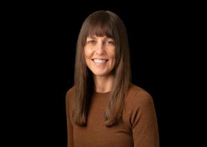 photo of a white woman smiling with brown hair in a brown shirt