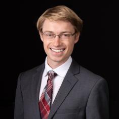 a white man in a red tie against a dark background